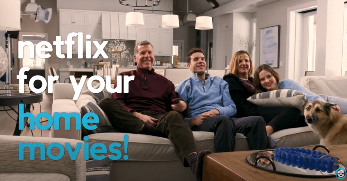 A smiling family of four and a dog sit on a couch in a modern living room, watching TV on their Smart TV. Text over the image reads, Netflix for your home movies!.